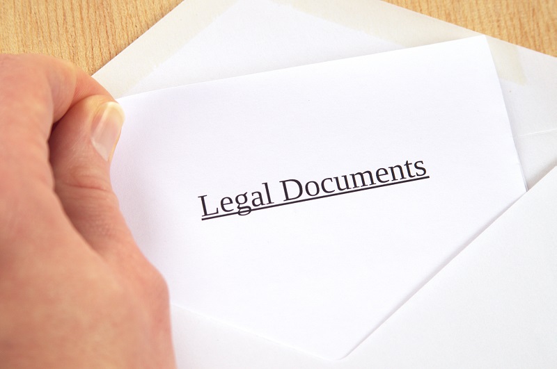 a hand holding a white envelope with black text. Containing the words: legal documents