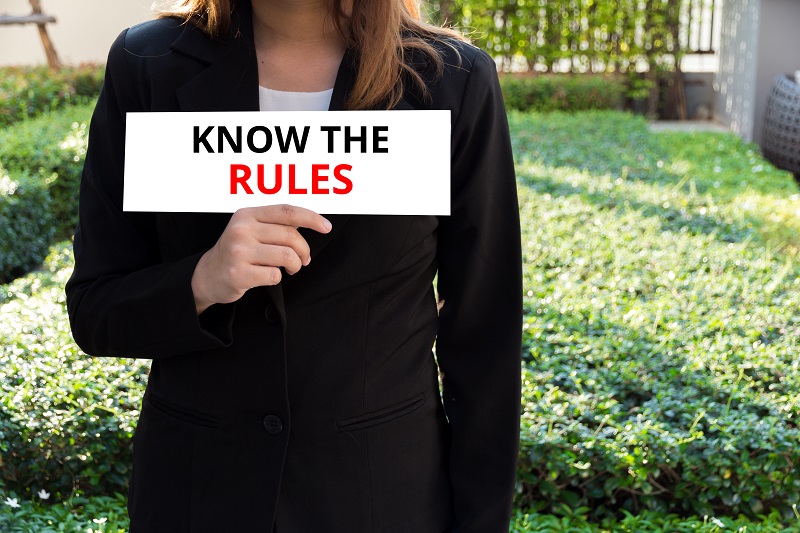 a person holding a sign. Containing the words: know the rules