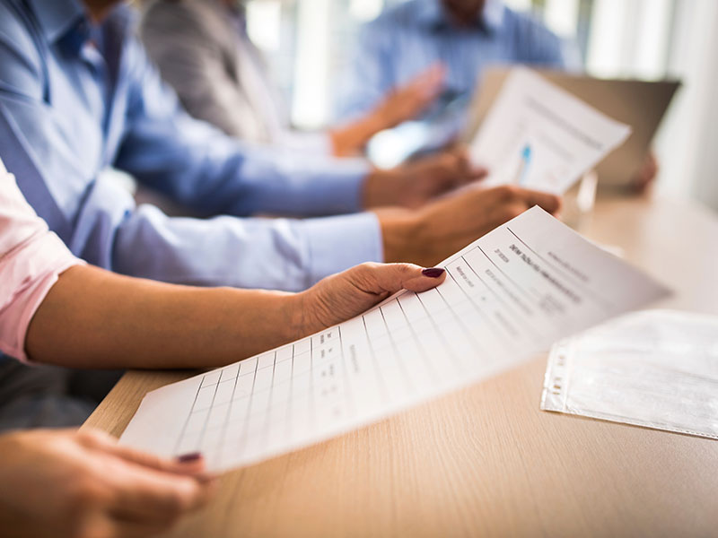 a group of people sitting at a table holding papers.