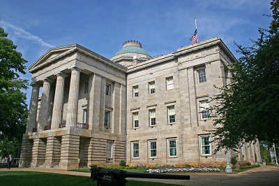 a large stone building with columns with North Carolina State Capitol in the background.