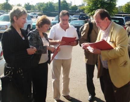 a group of people standing outside looking at papers.