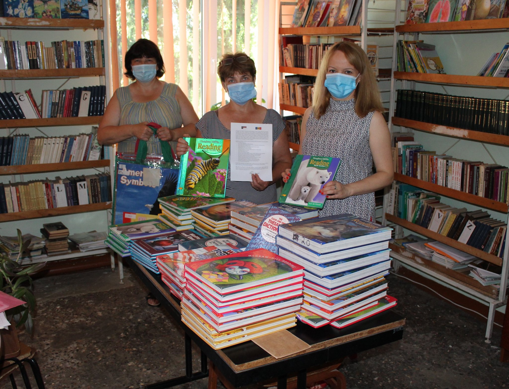 a group of women wearing face masks standing in front of a table with books.